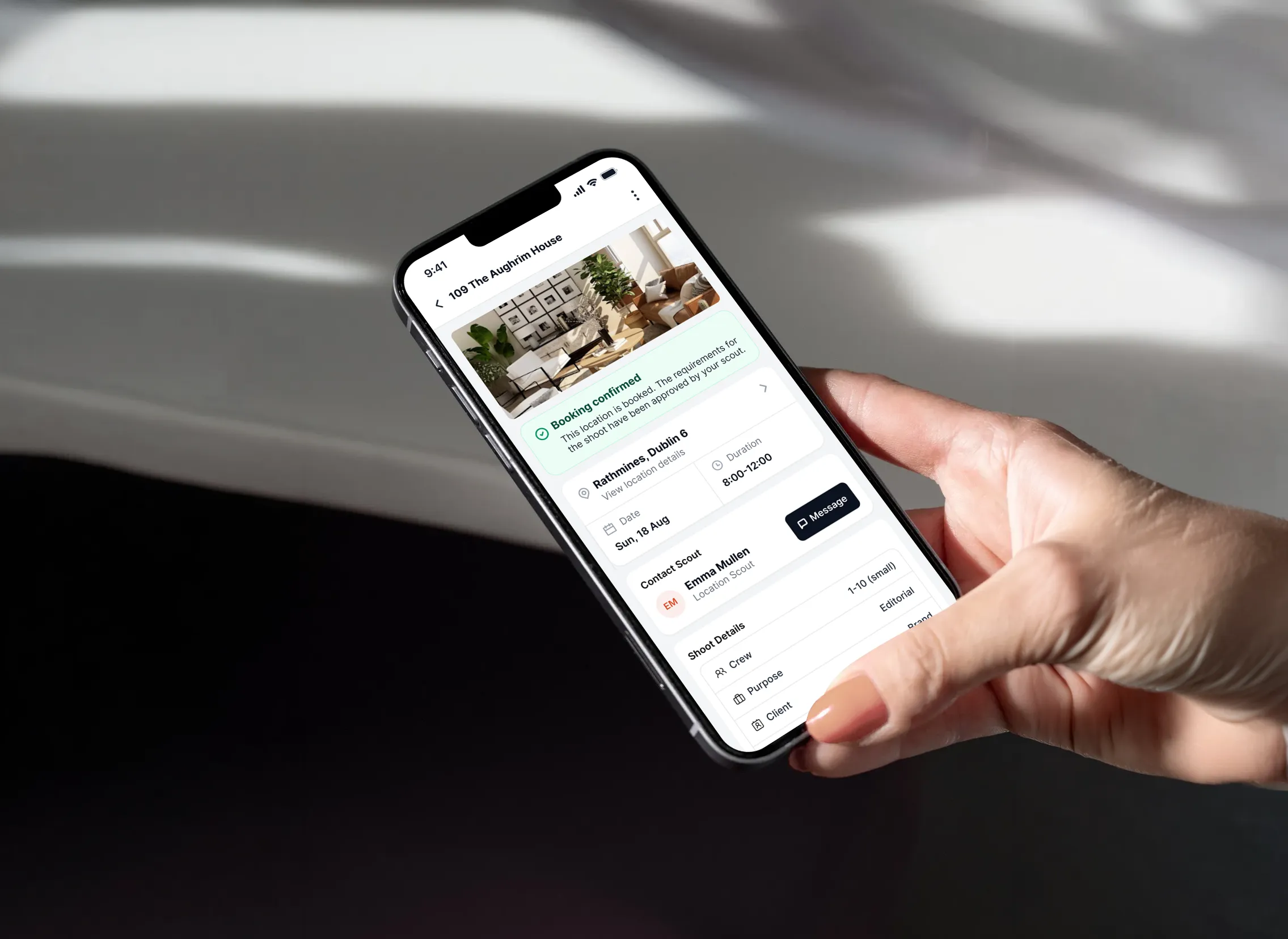 Hand holding a phone showing a confirmed booking, with location details and the assigned scout's contact.